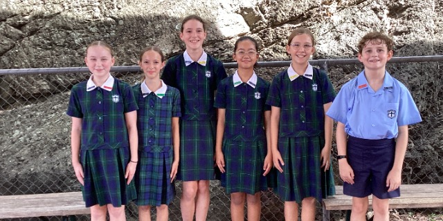 Students in school uniform posing together outdoors near a rock wall.