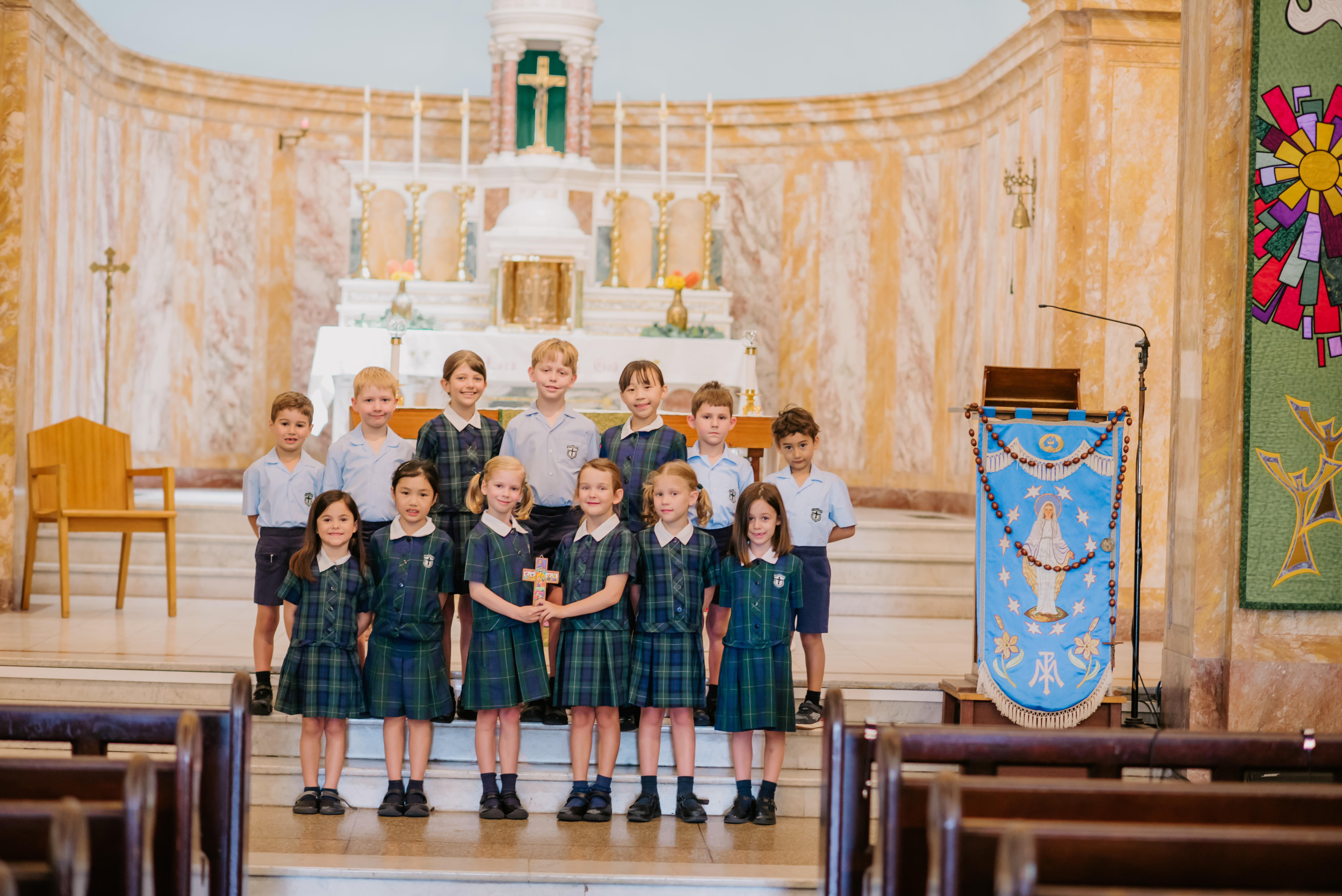 Students in school uniform standing together at the front of a church near the altar.