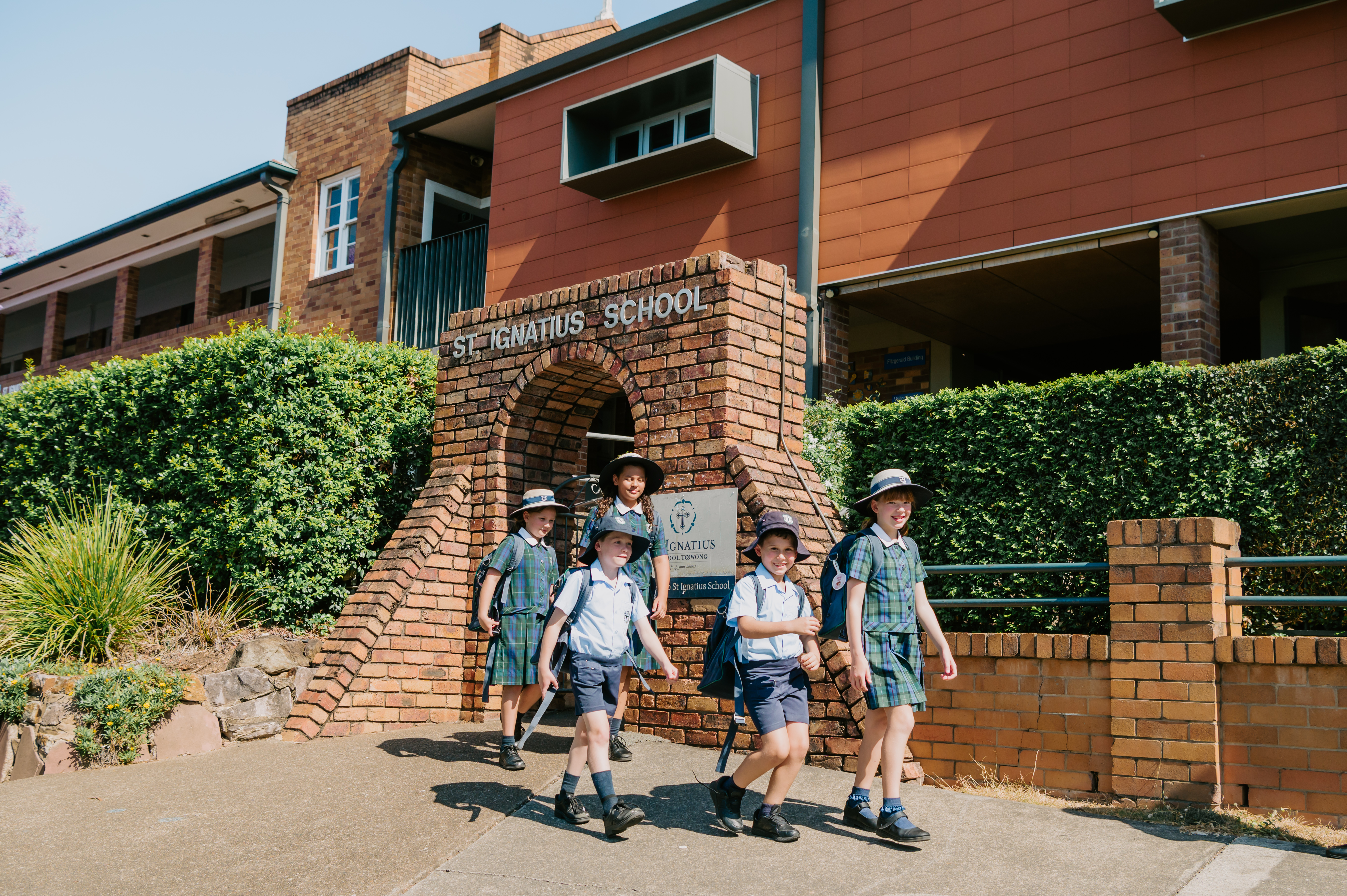 Students in school uniform walking past the brick entrance sign for St Ignatius School.